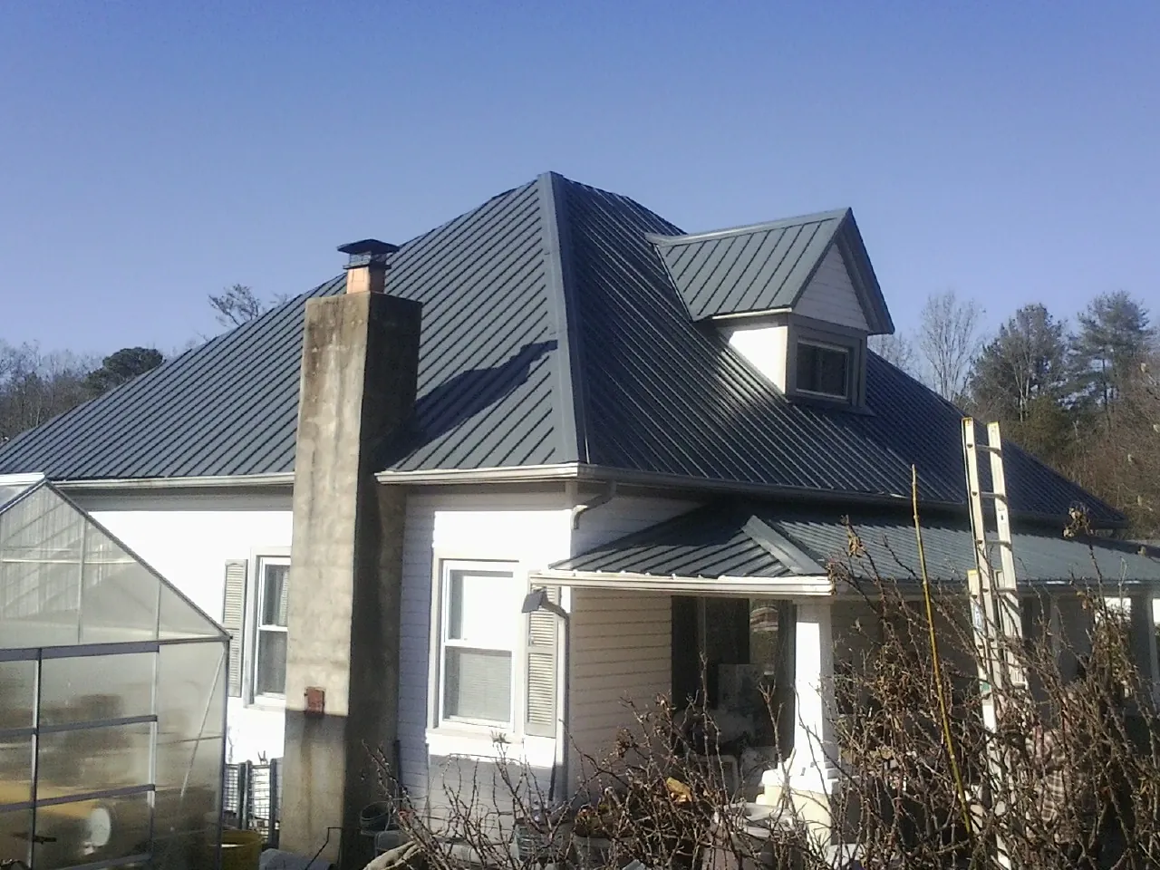 Dark blue standing seam metal roof on a white farmhouse with dormer — Slate & Tile Roof Repair by Roofing Brothers in Lexington
